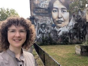 Selfie of Nathalie in front of suffragette mural on side of Lord Morpeth pub in Bow.